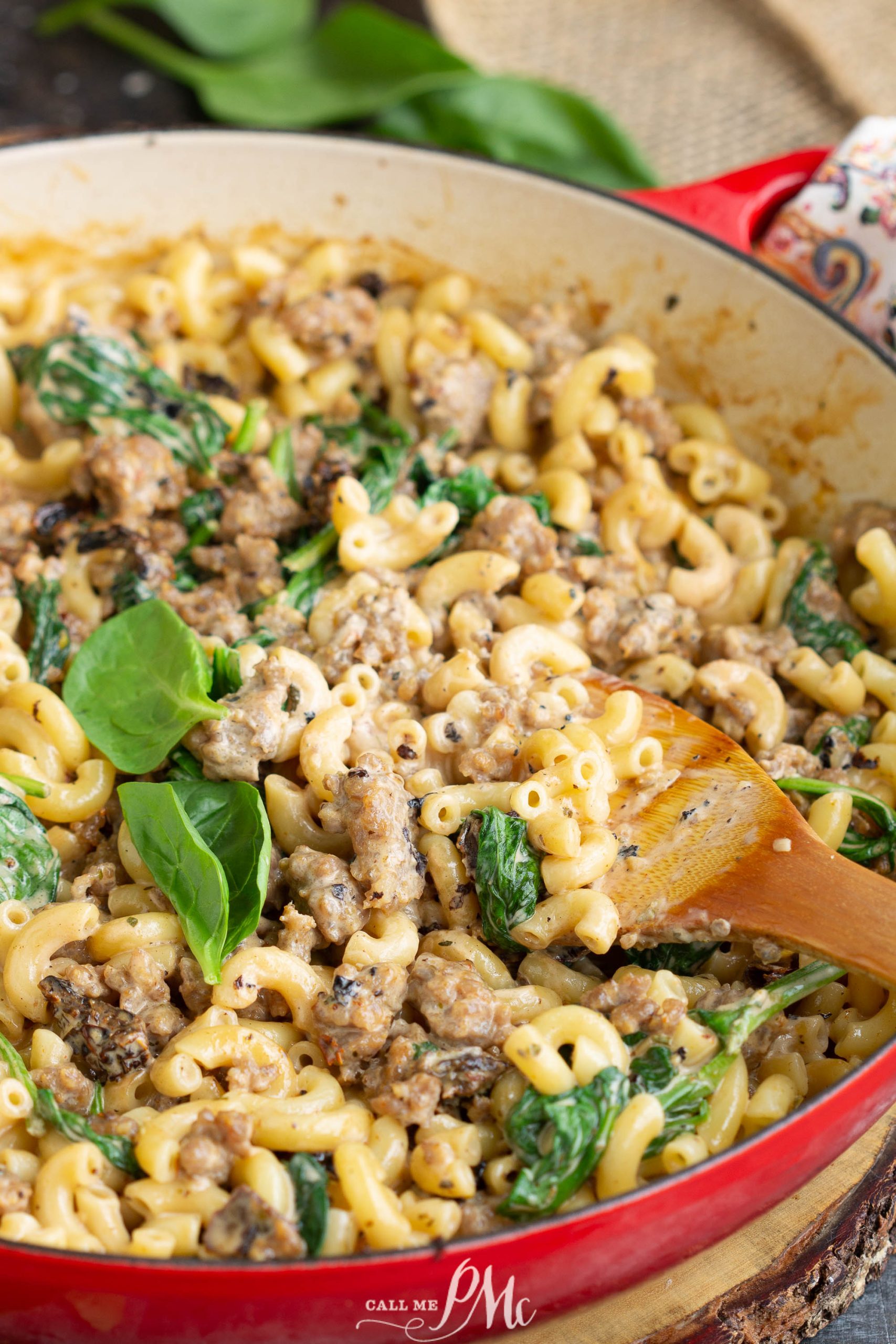 Italian sausage and spinach are cooked together with mac and cheese in a red skillet to create a delicious and flavorful Italian Sausage Pasta dish.