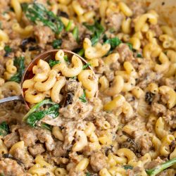 Italian sausage mac and cheese with spinach cooked in a red skillet.