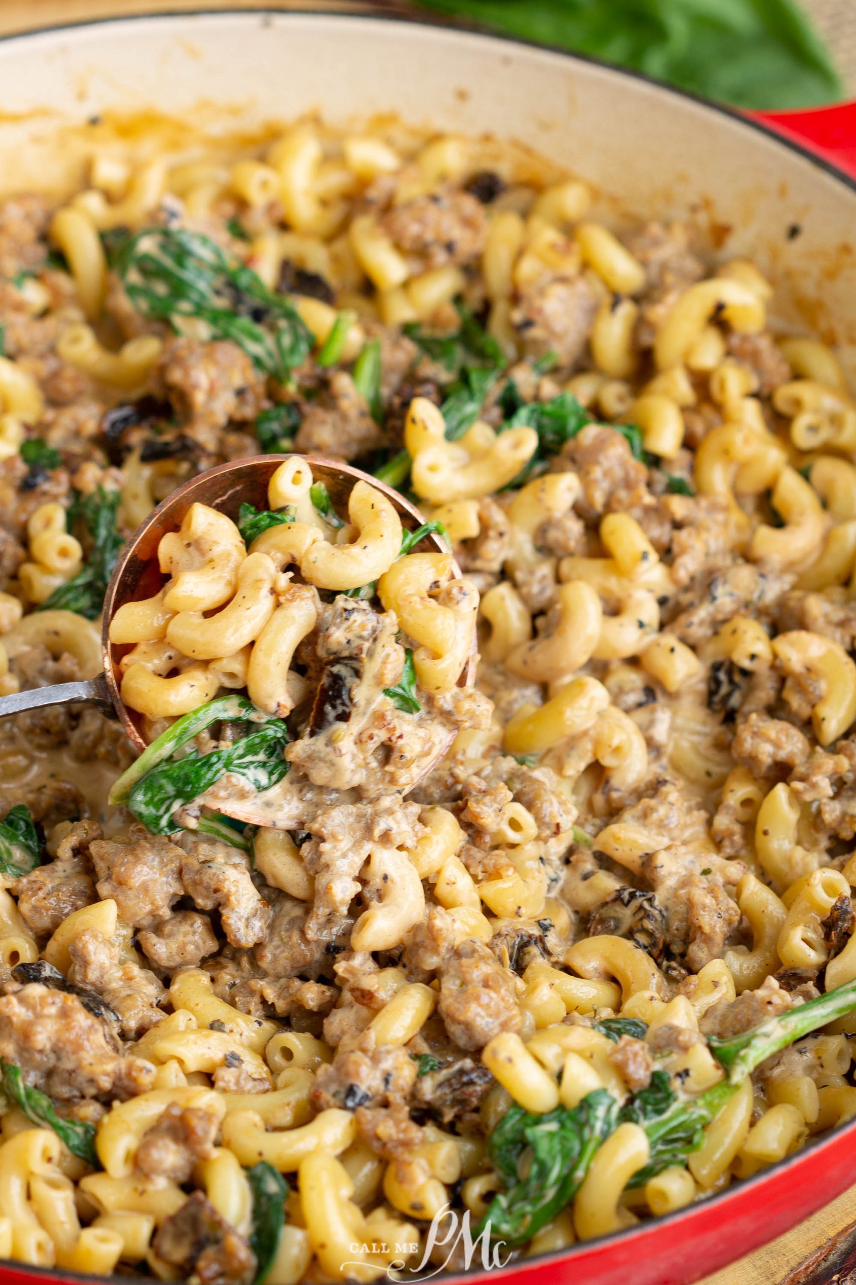 Italian sausage mac and cheese with spinach cooked in a red skillet.