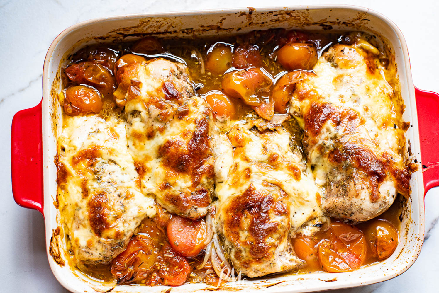 Chicken covered with cheese in a casserole dish with roasted tomatoes.