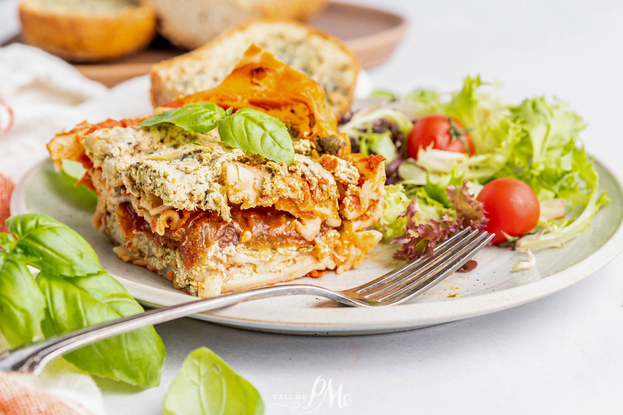 Veggie lasagna on a plate with a salad and fork.