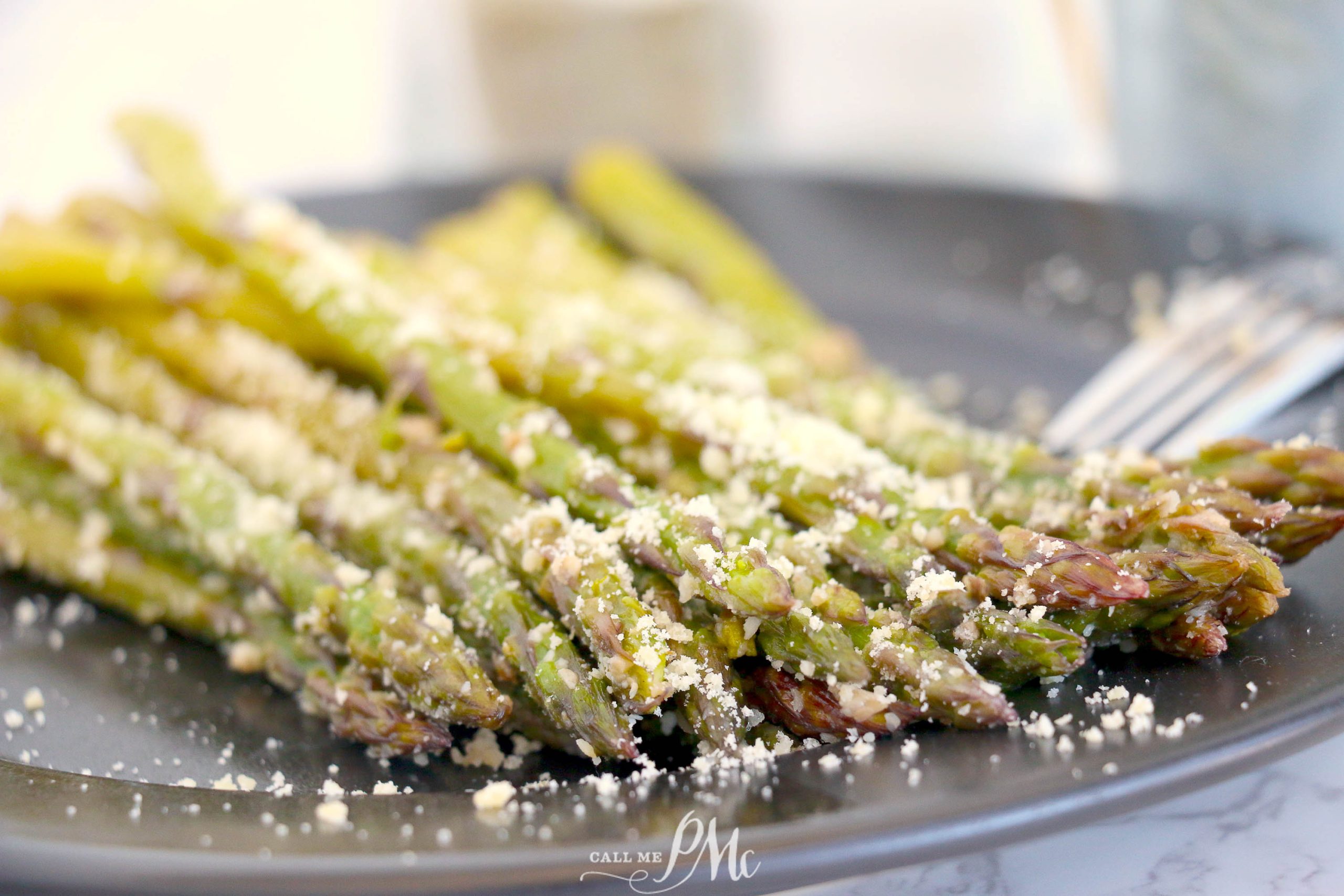 Asparagus on a black plate with parmesan cheese.