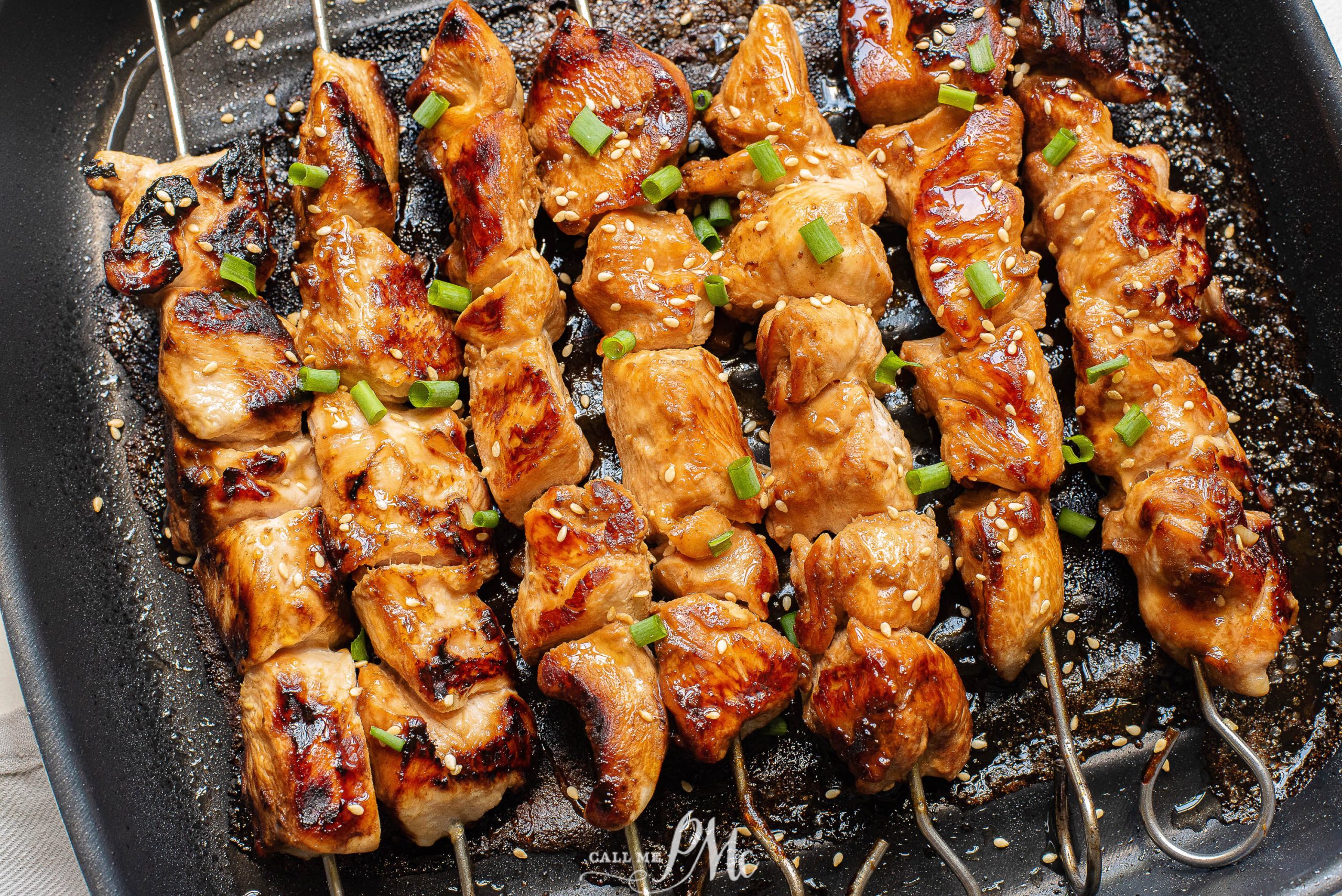 Cooked chicken chunks on skewers in a grill pan.