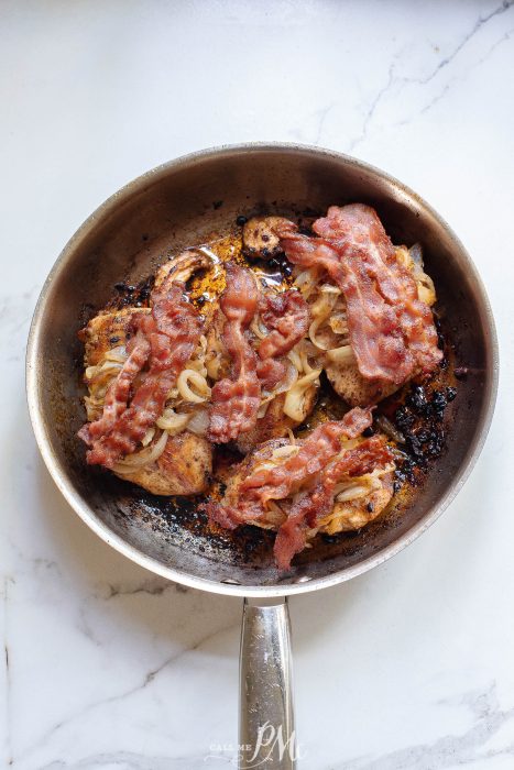 chicken topped with onions and bacon in pan