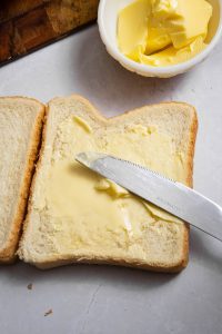 A slice of white bread with butter and a butter knife on a plate.