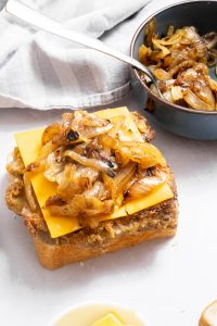 Slice of bread with fried steak, cheese and caramelized onions on it.