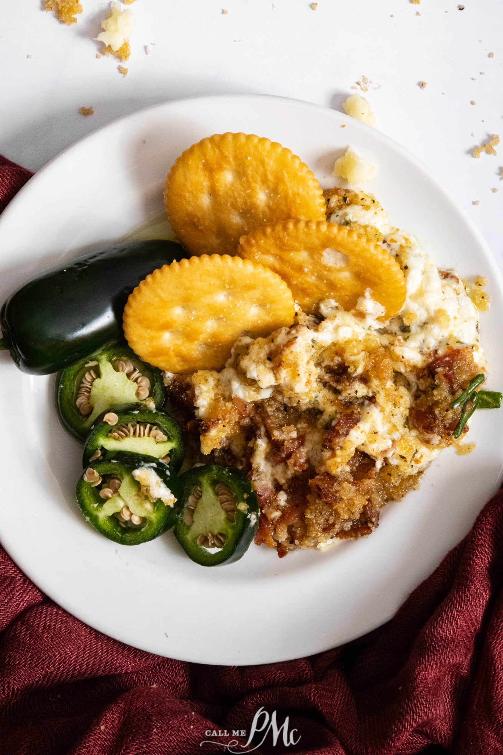 A white plate with japapeno popper dip, jalapenos, and crackers.