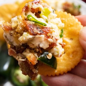 A hand holding round cracker with dip on it.