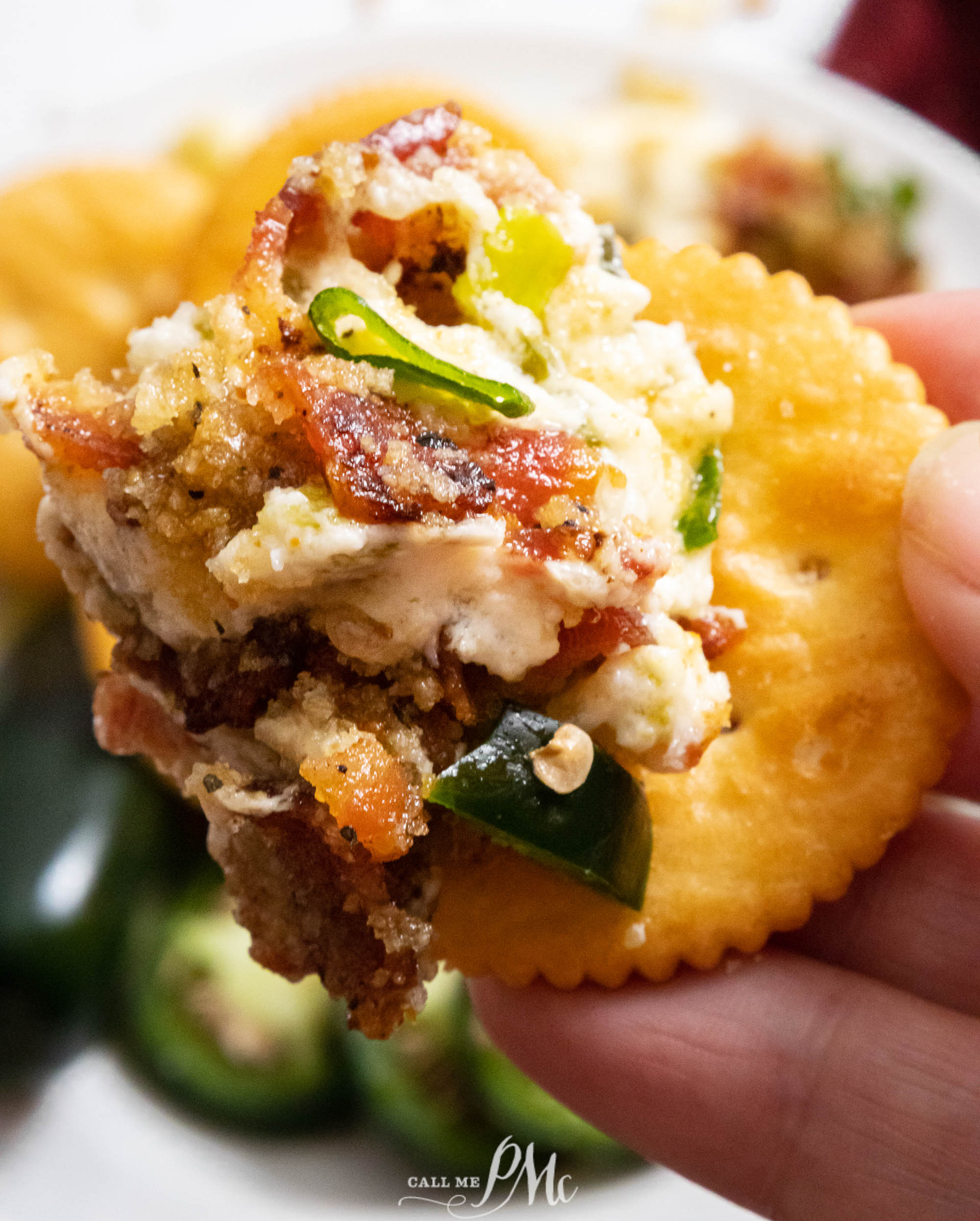 A hand holding round cracker with dip on it.