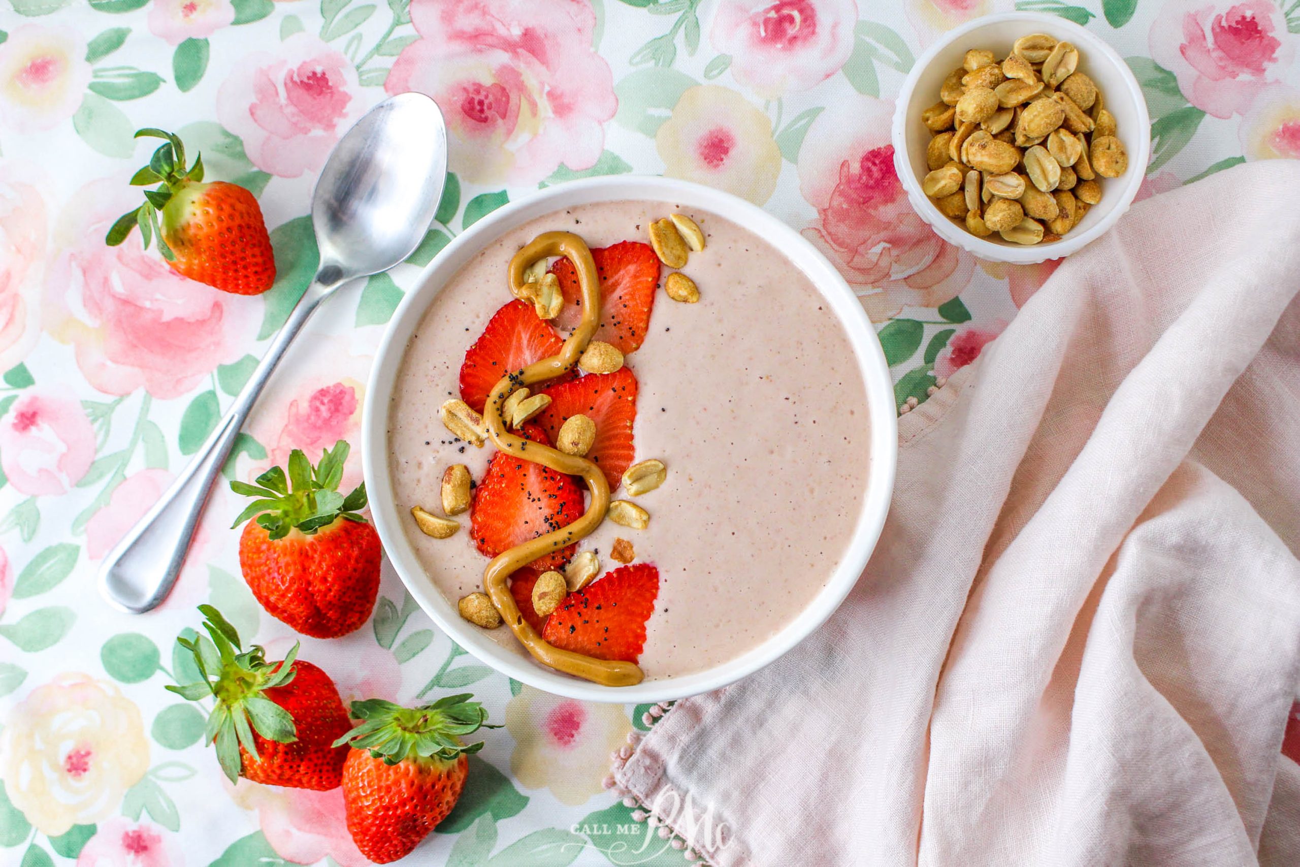 Smoothie topped with strawberries, peanuts, and peanut butter swirl in bowl.