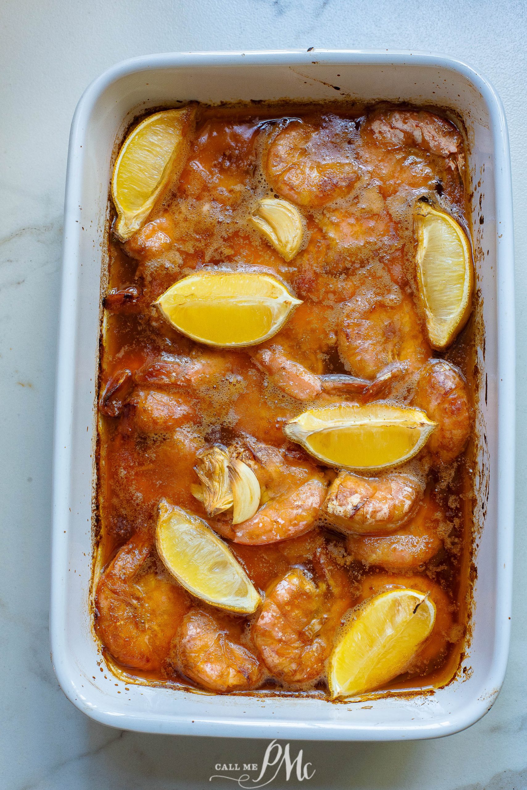 Shrimp in red sauce with lemon wedges in a casserole dish.
