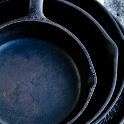 Flatlay of four seasoned cast iron skillets.