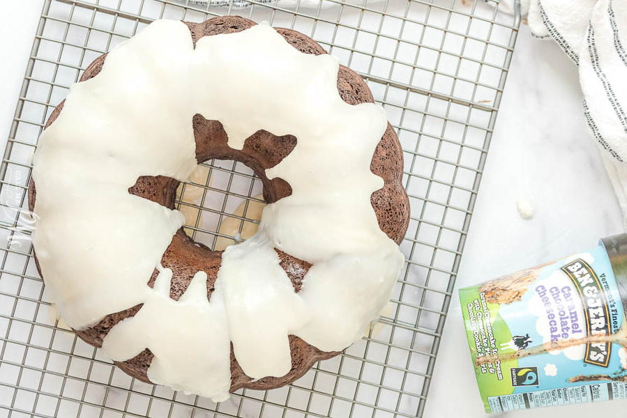 Flatlay of chocolate bundt cake with off-white frosting dripping of the cake on a wire rack.