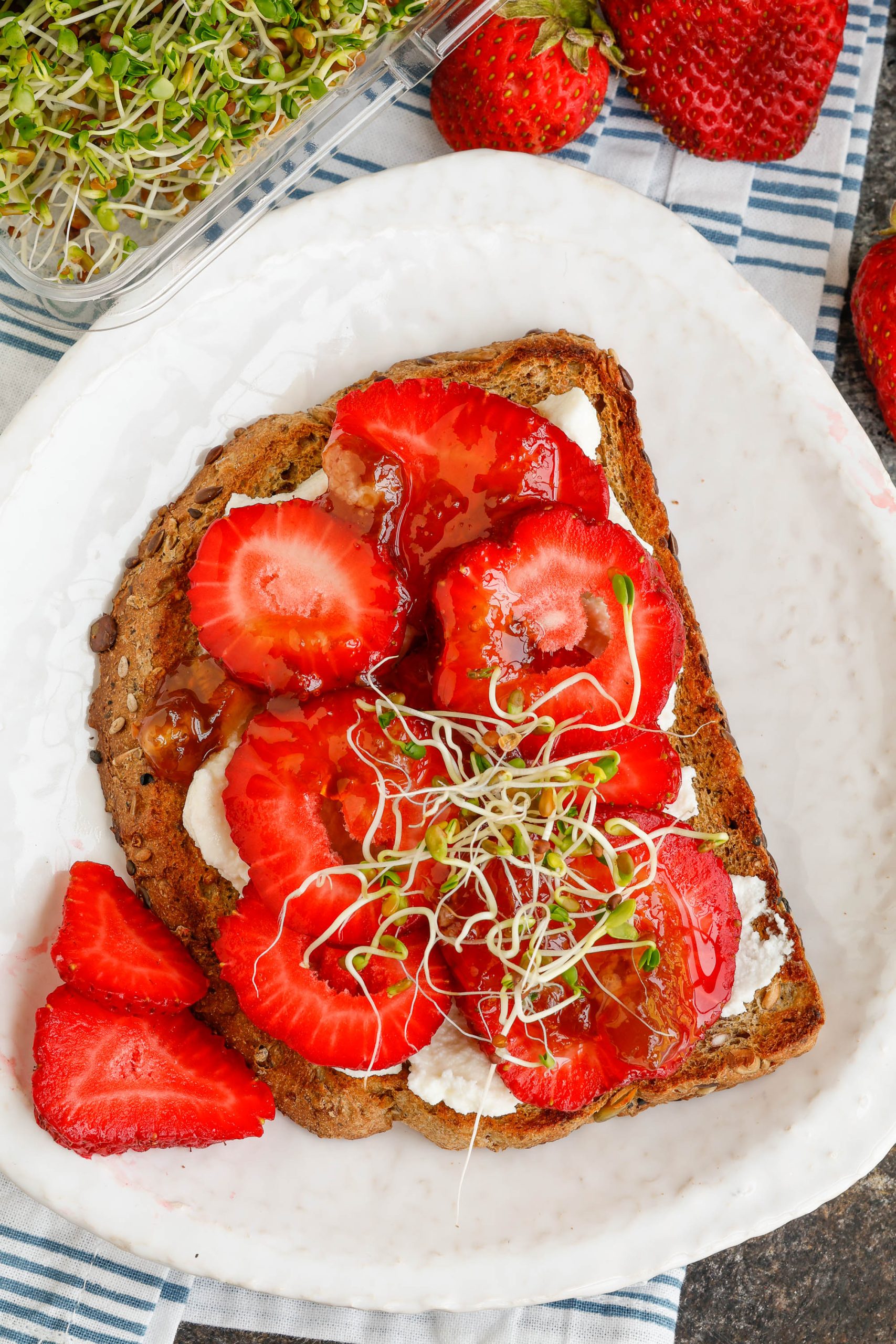 Strawberries, jam, and sprouts on toasted bread.