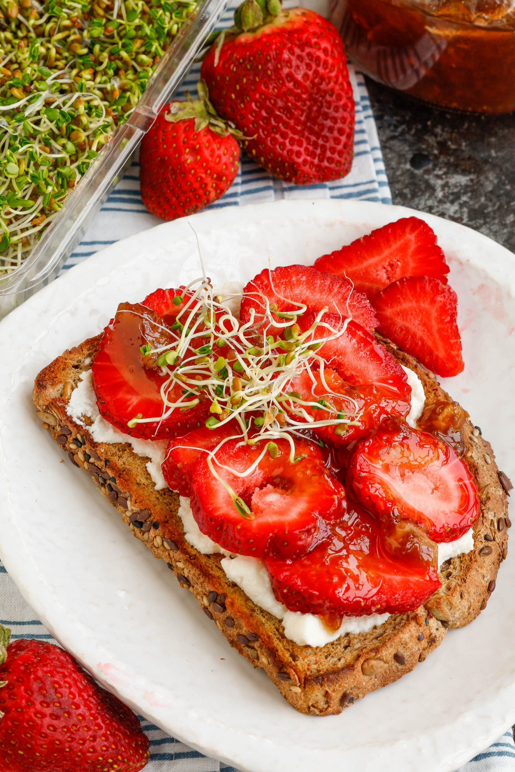 Strawberries, jam, and sprouts on toasted bread.