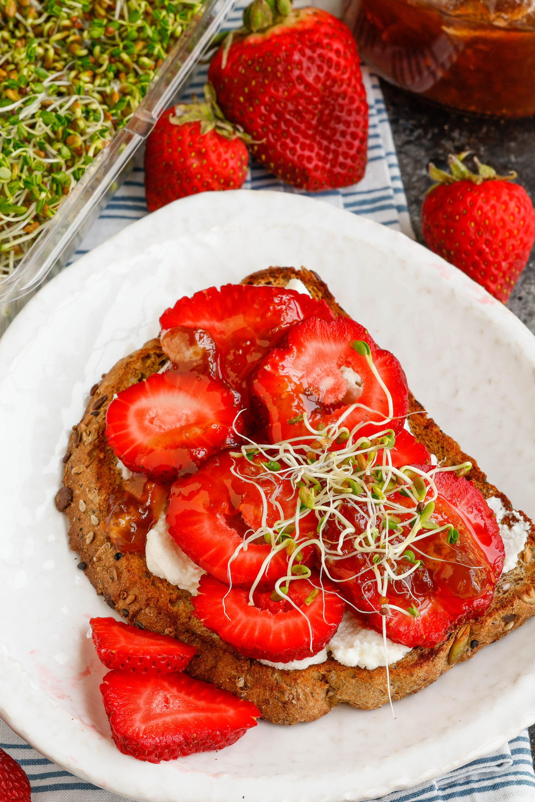 Strawberries, jam, and sprouts on toasted bread.