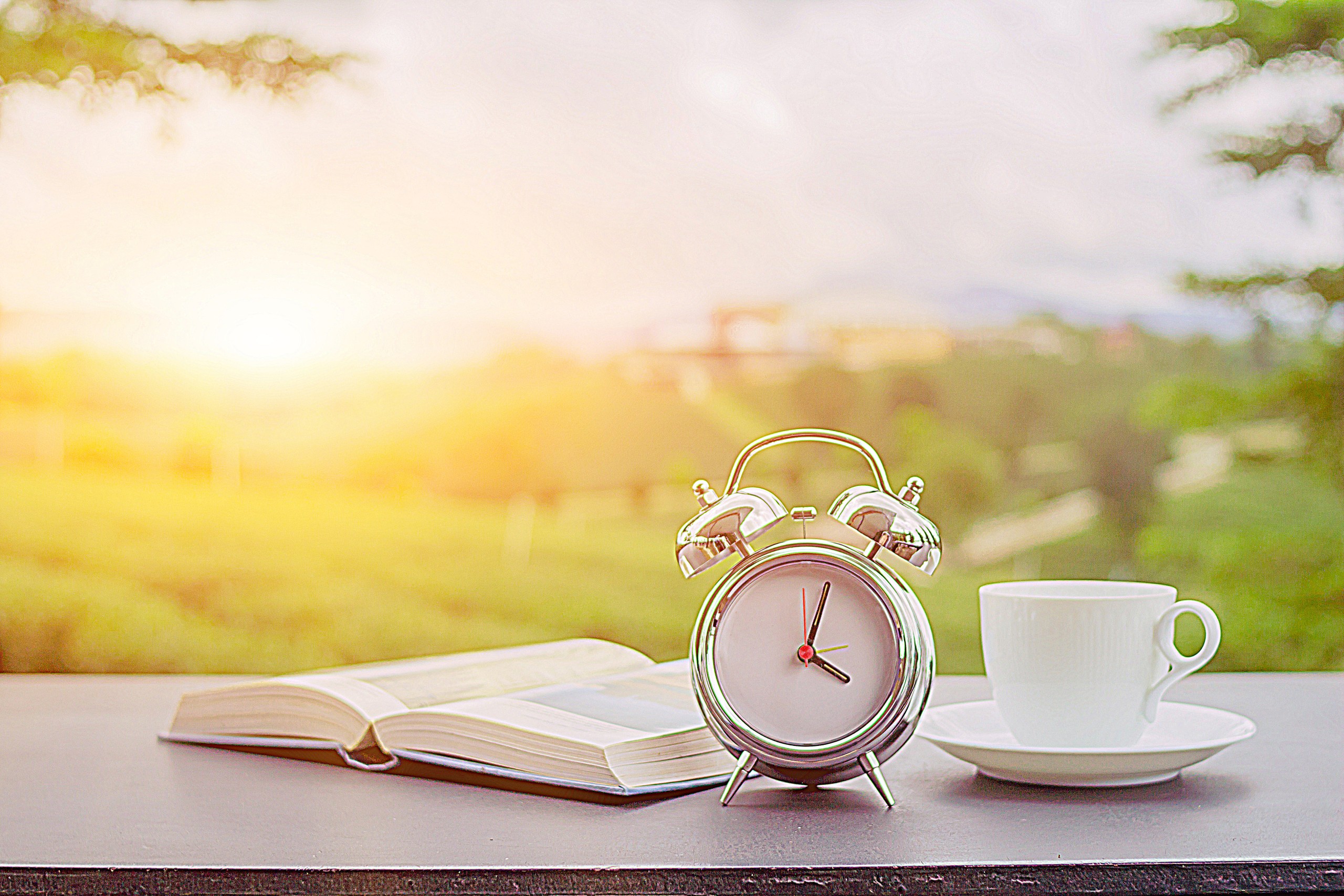 Clock on table outside with coffee and open book.