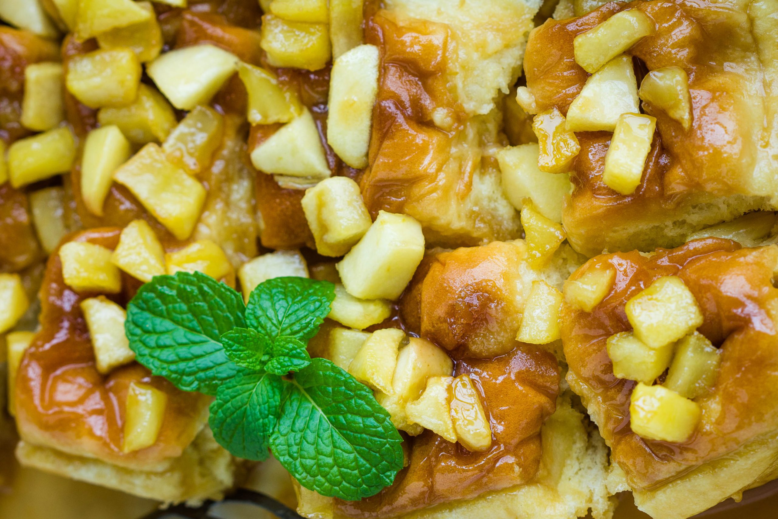 A plate of sticky buns with apples and a mint leaf on it.