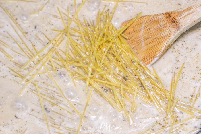 A wooden spoon is being used to stir noodles in a pan.