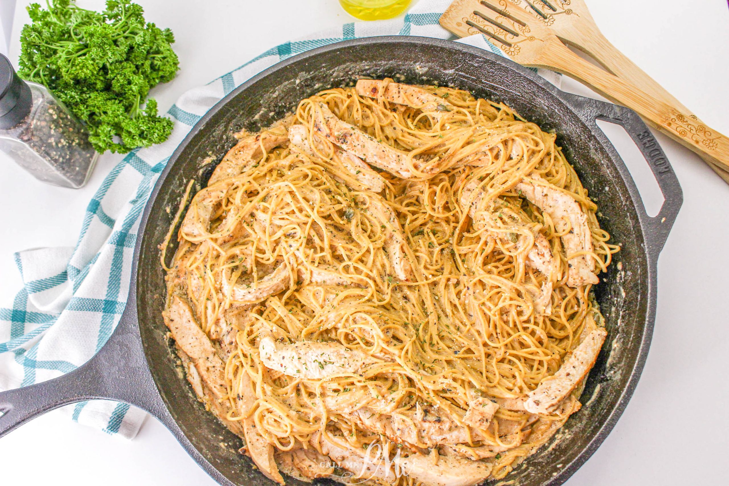 Chicken Caesar Angel Hair Pasta A skillet full of spaghetti with chicken and parsley.
