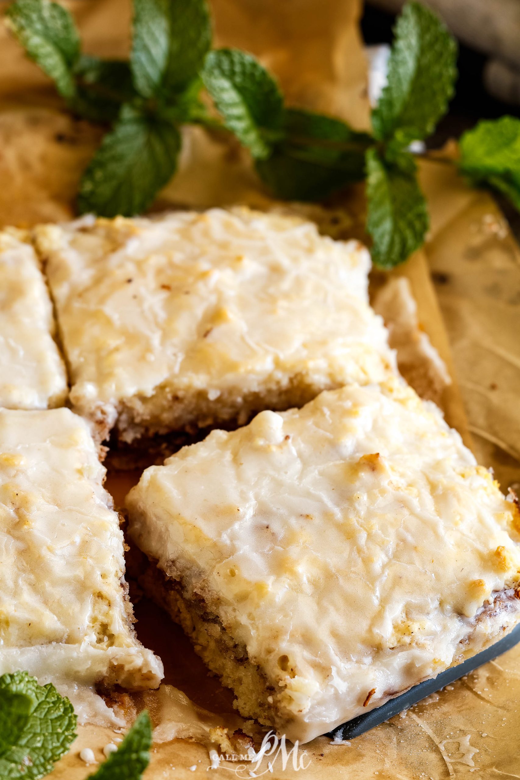 Lemon bars with icing and mint leaves on a baking sheet, in addition to cinnamon rolls.