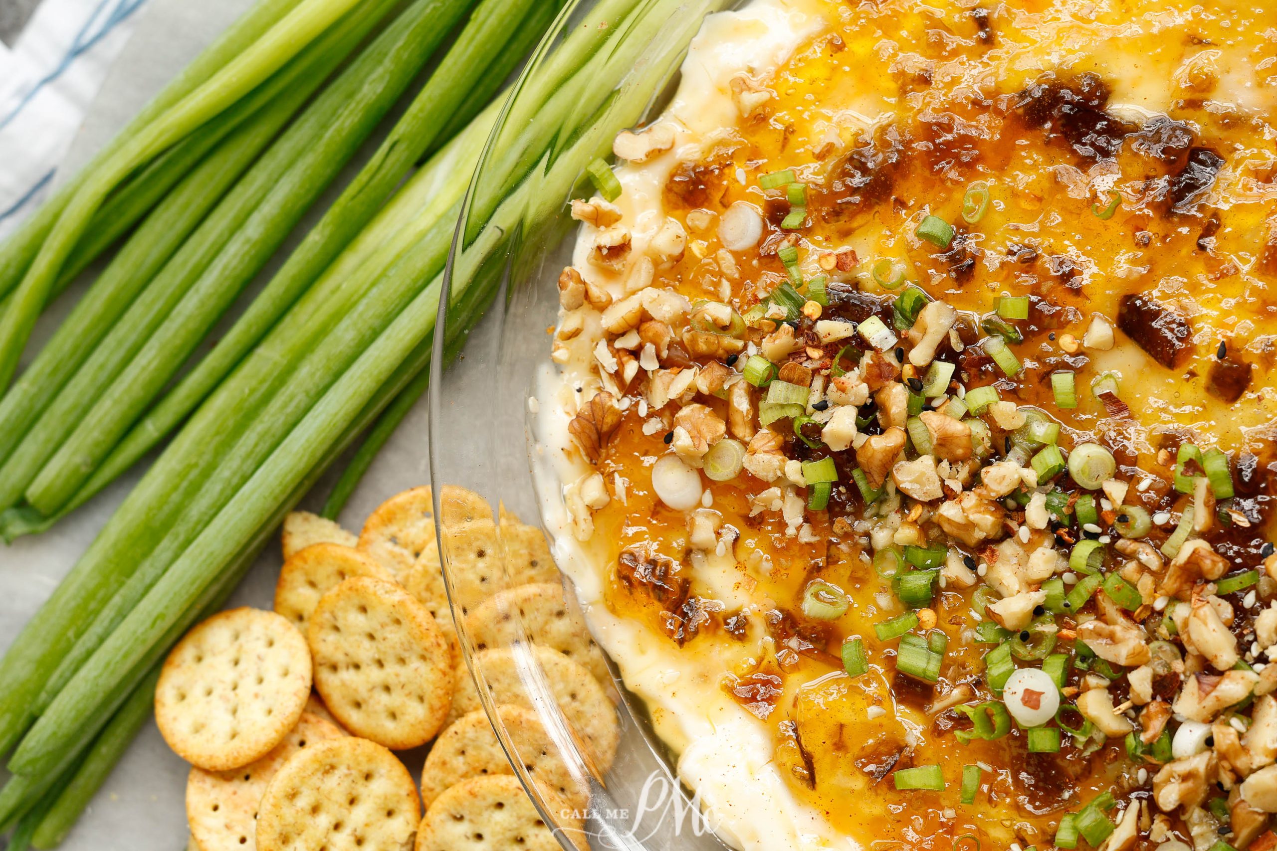 A bowl of cheese dip with crackers and green onions.