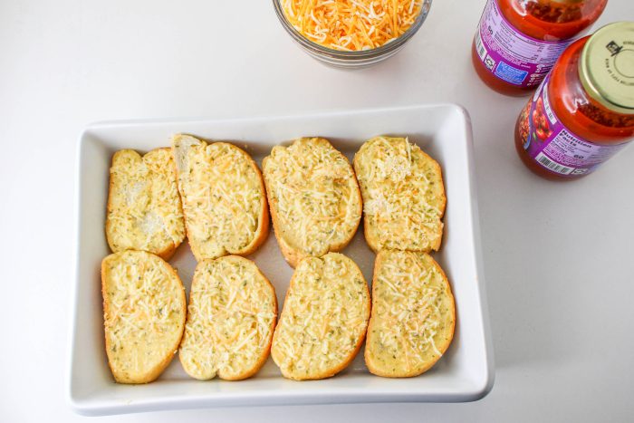 Cheesy garlic bread on a white plate next to a bottle of sauce.