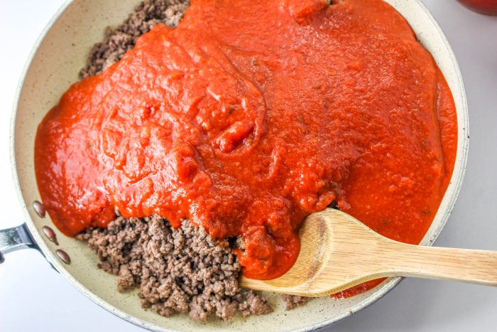 A pan with meat sauce and a wooden spoon.