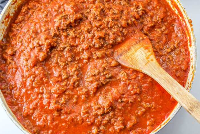 Meat sauce in a pan with a wooden spoon.