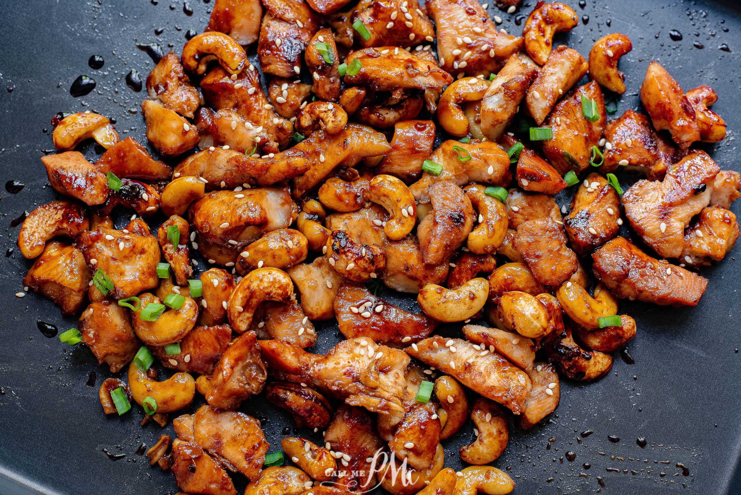 Cashew chicken on a black pan with sesame seeds.