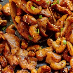 Chicken and cashews in a pan with a wooden spoon.