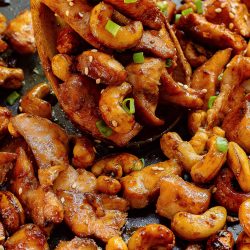 Chicken and cashews in a pan with a wooden spoon.