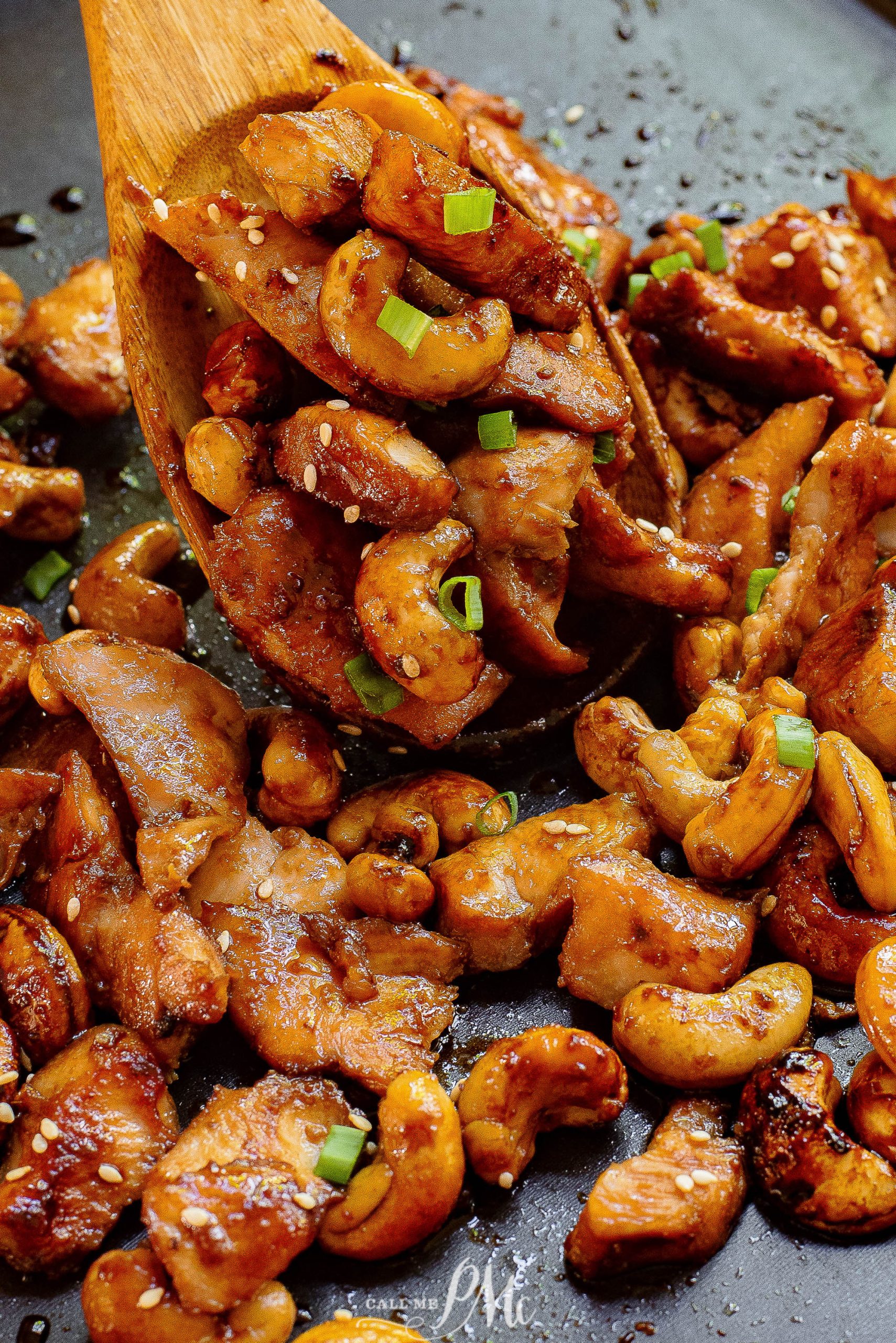 Chicken and cashews in a pan with a wooden spoon.