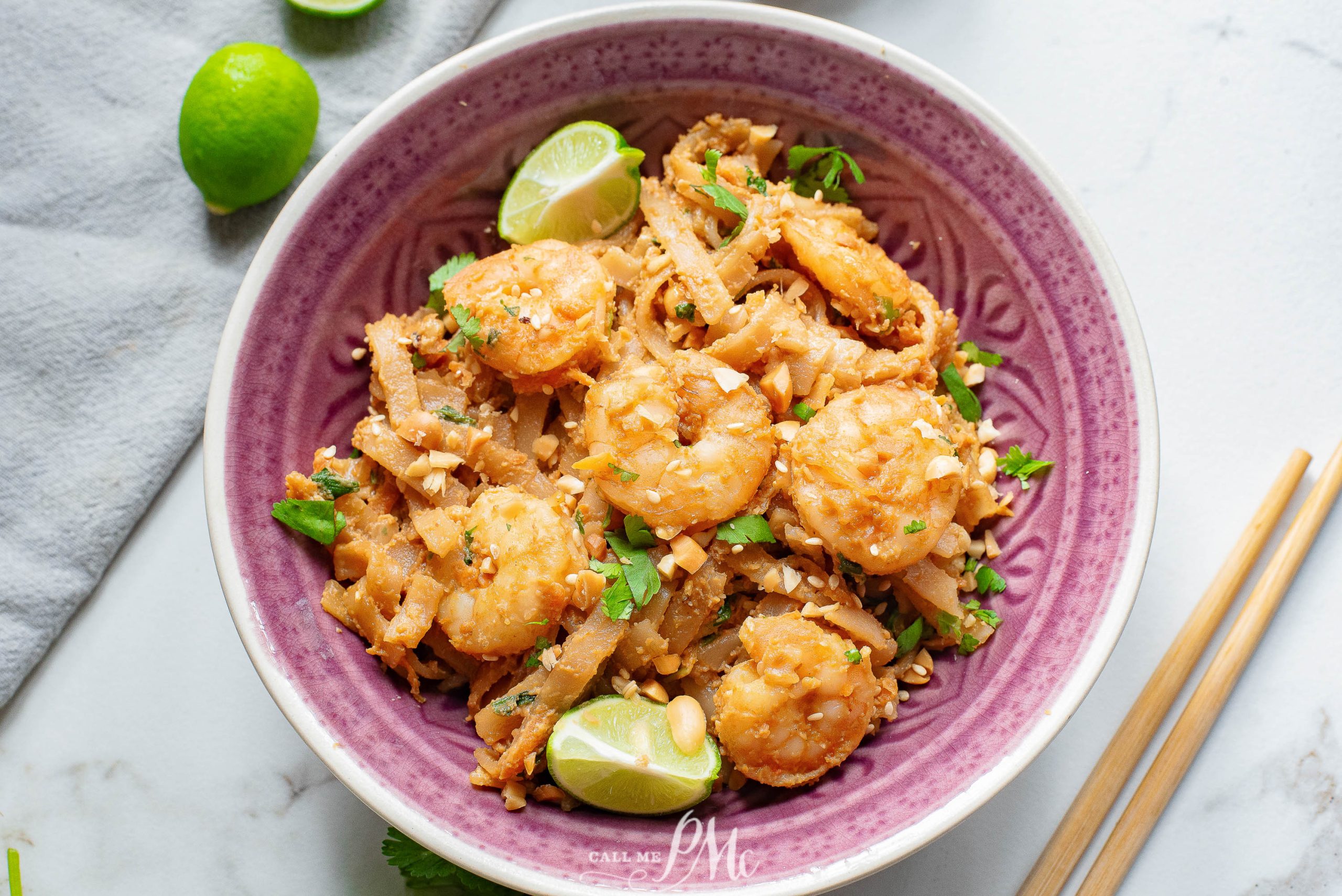 Thai shrimp pad thai in a bowl with limes and chopsticks.