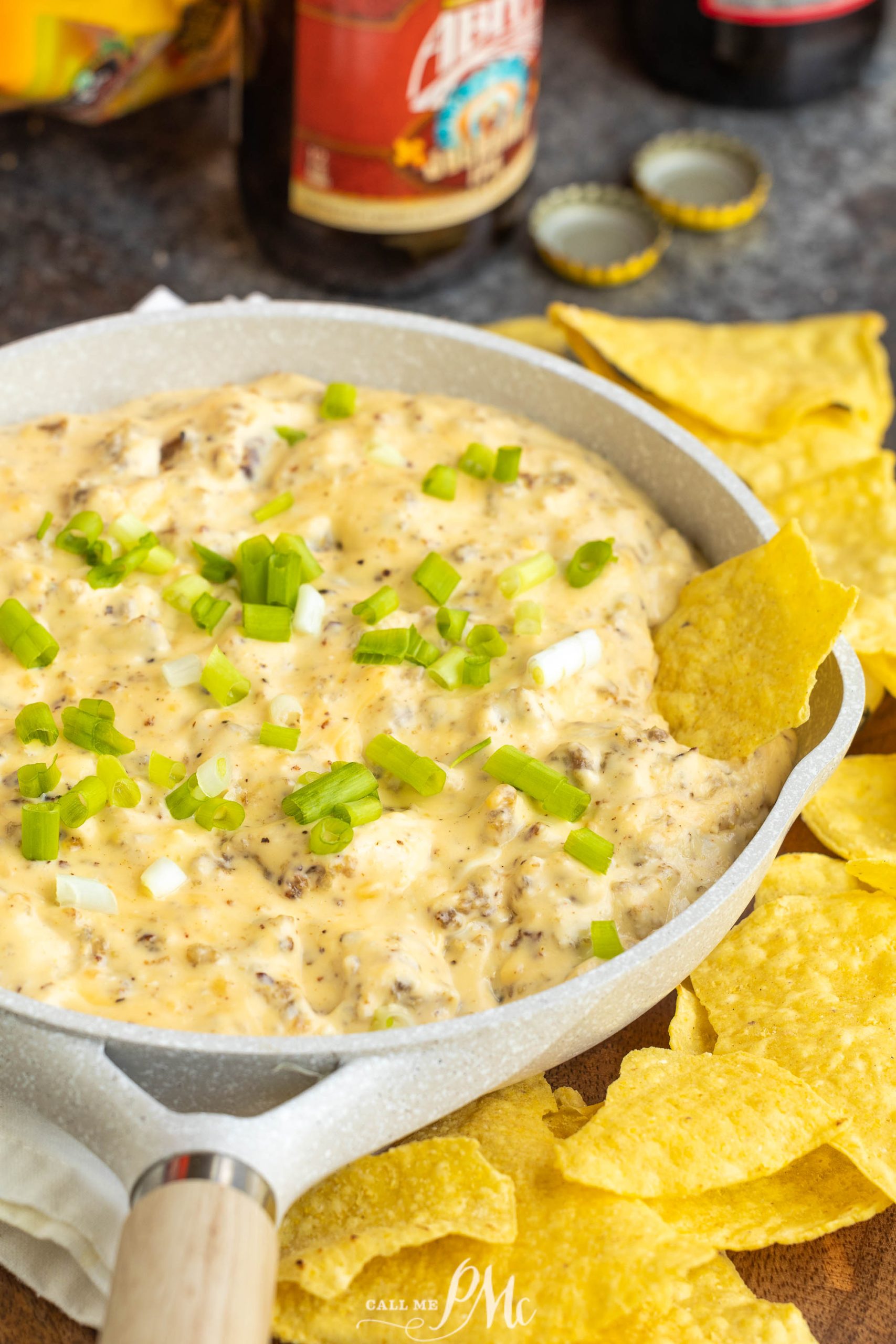 Cheesy nacho dip in a skillet with chips and beer.