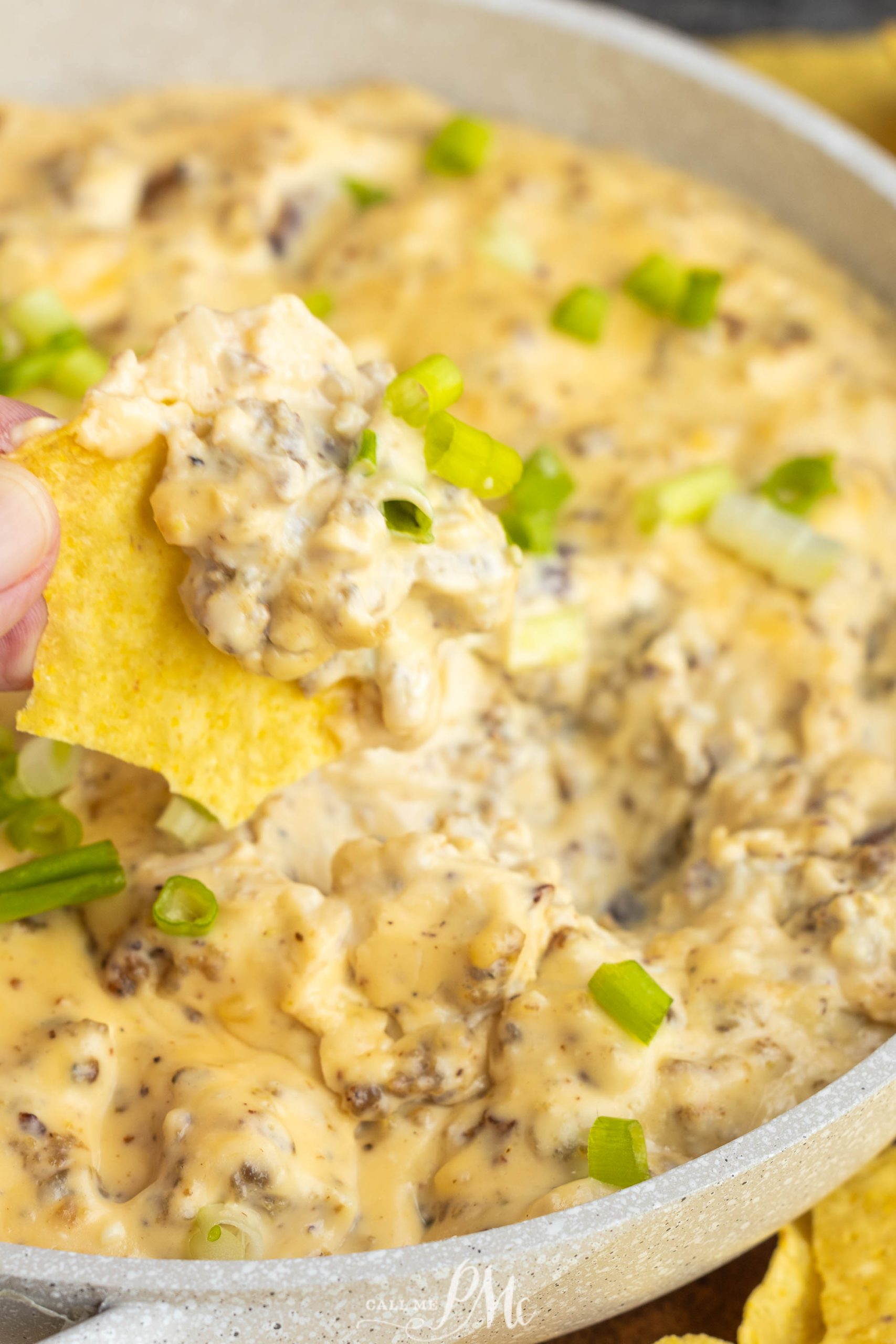 A person dipping a chip into a bowl of cheese dip.