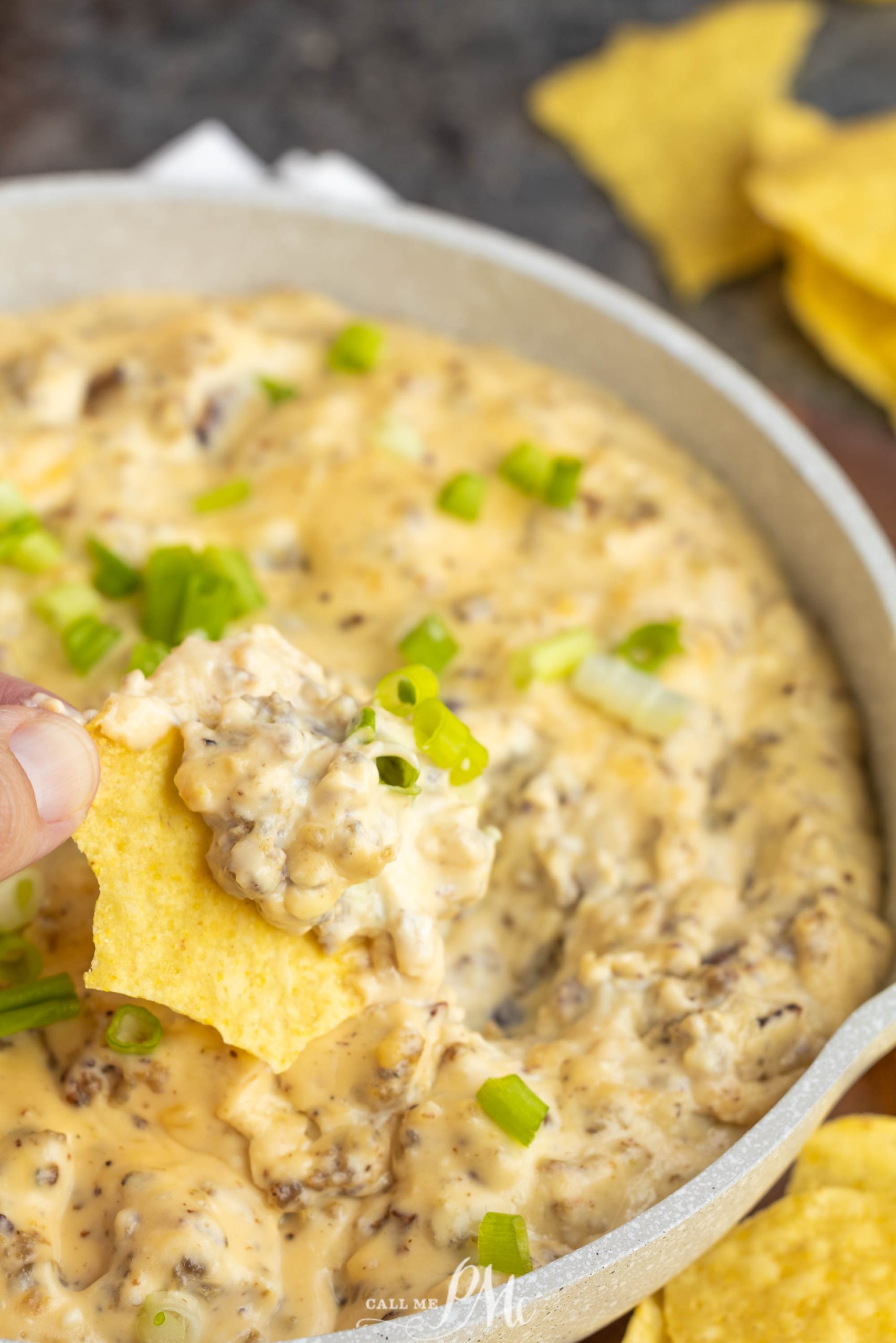 A person dipping a tortilla chip into a bowl of cheese dip.