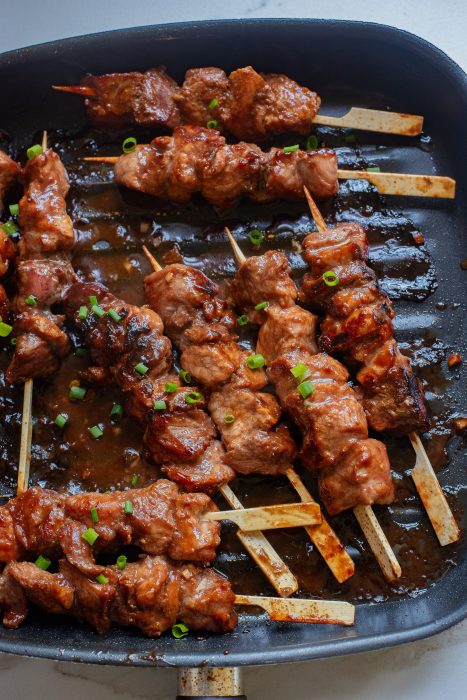 Meat skewers in a pan with sauce on them.