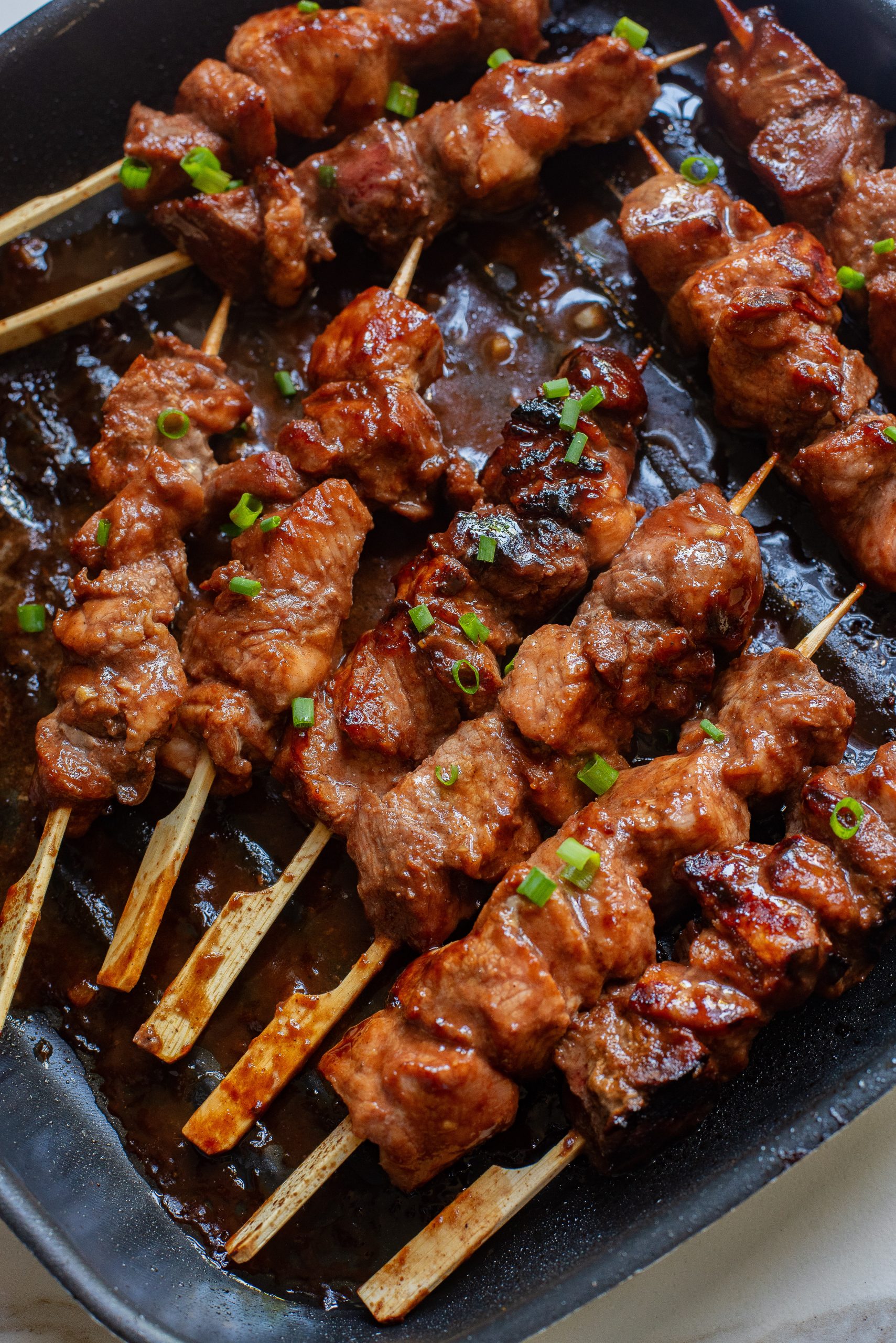 Hoisin Pork Tenderloin on skewers in a pan.