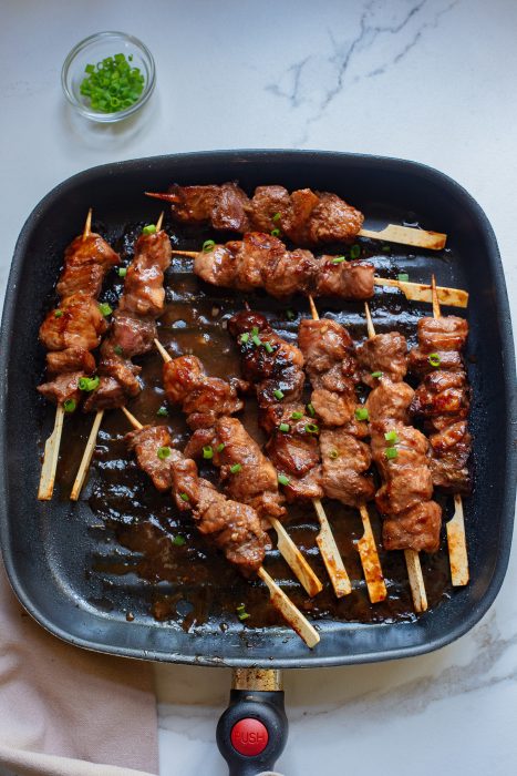 Hoisin Pork Tenderloin on skewers in a pan.