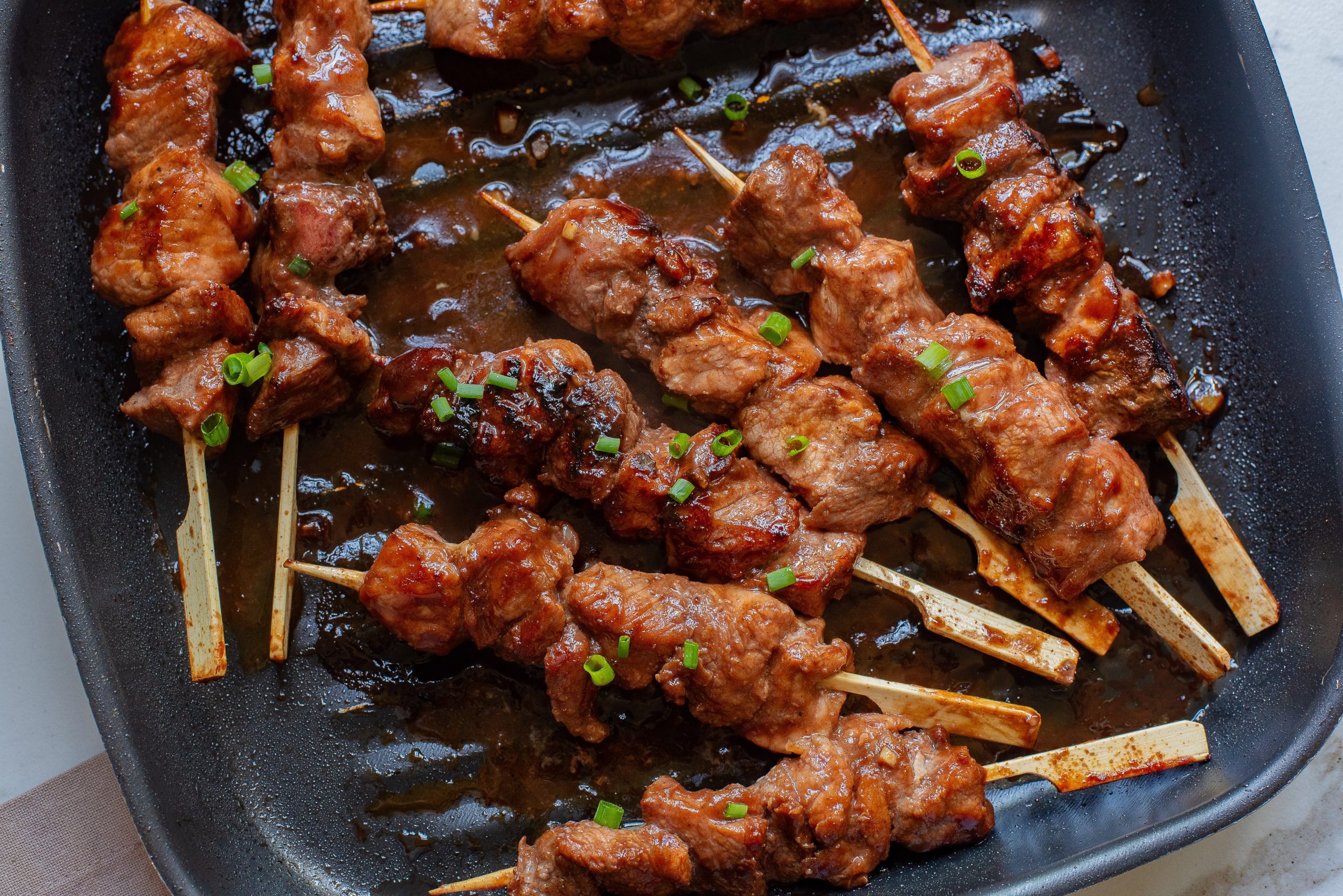 Hoisin Pork Tenderloin on skewers in a pan.