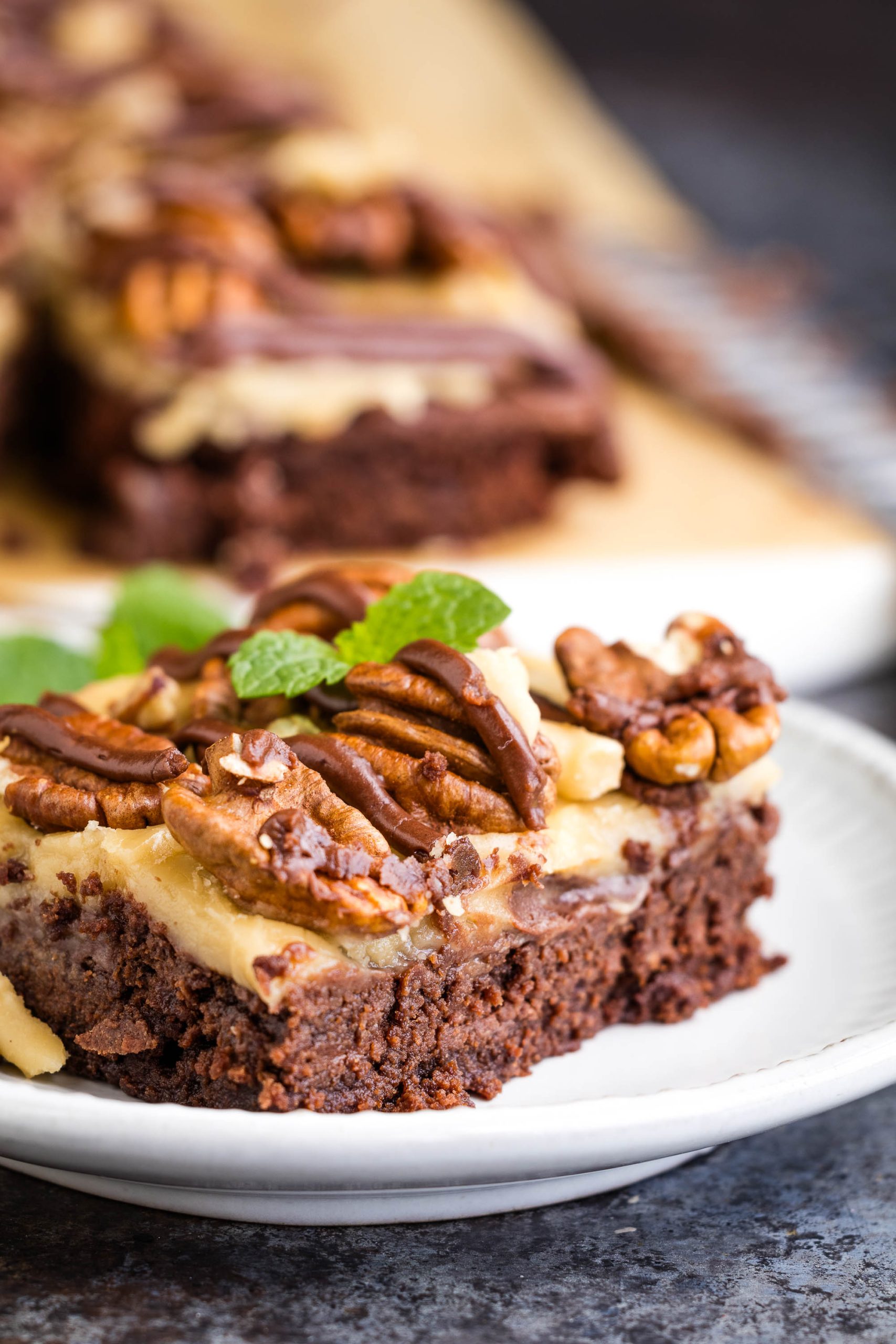 A piece of brownie with pecans and mint on a plate.
