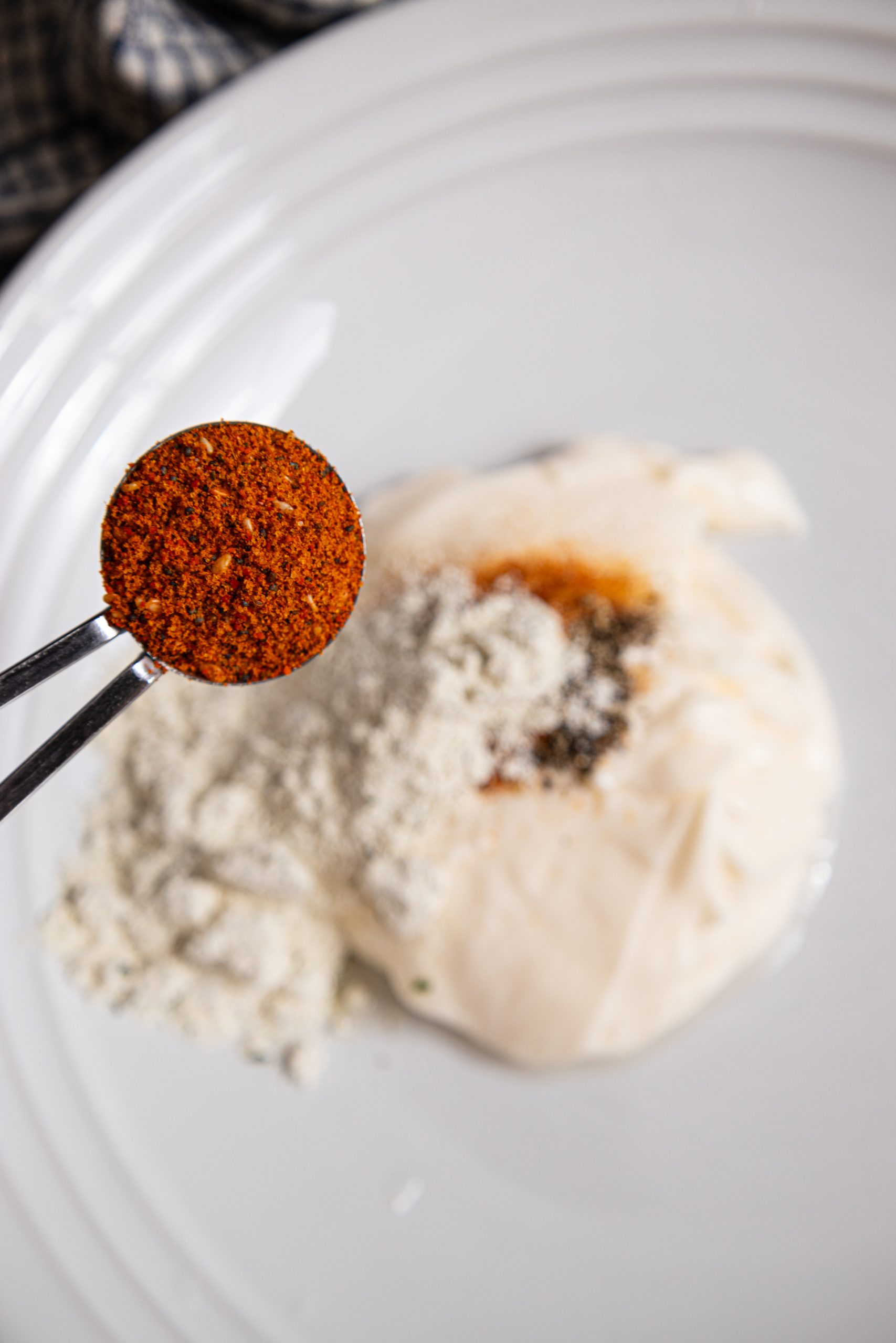 A spoon is holding a small amount of spice on a white plate.
