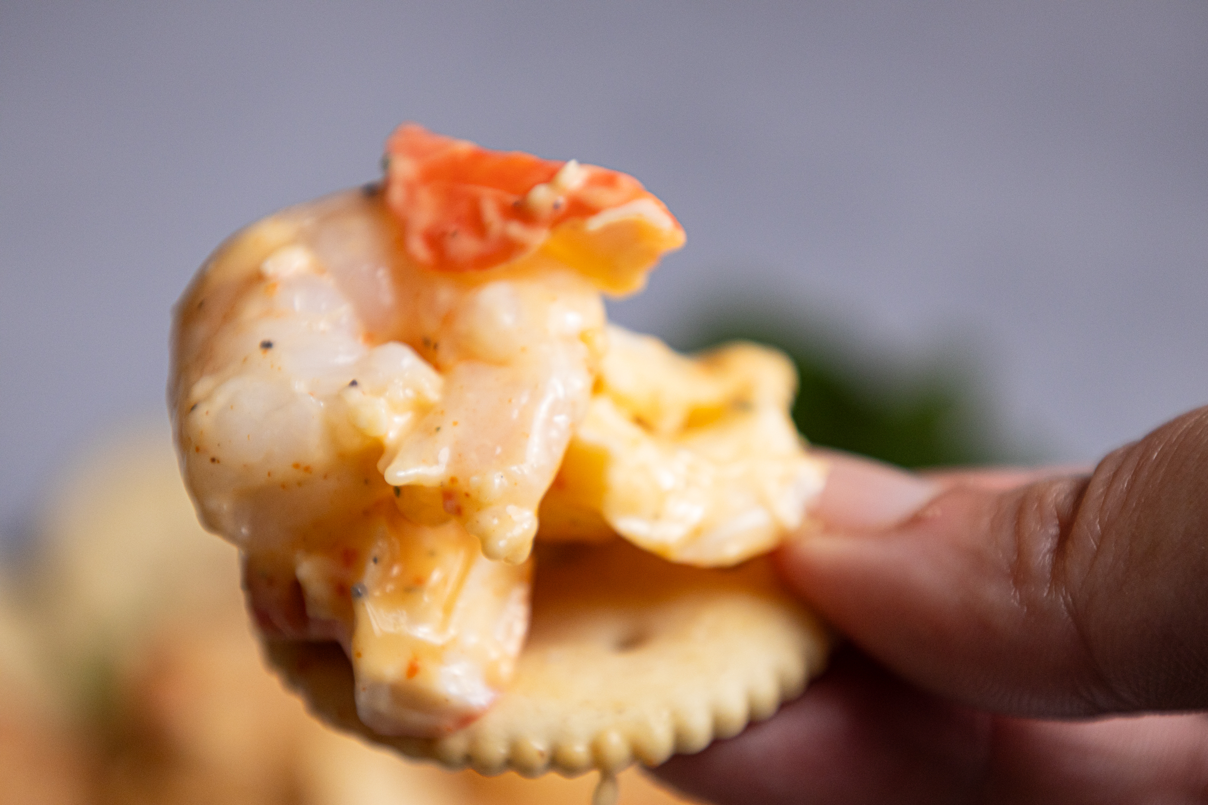 A person holding a cracker with Light Shrimp and Crab Remoulade