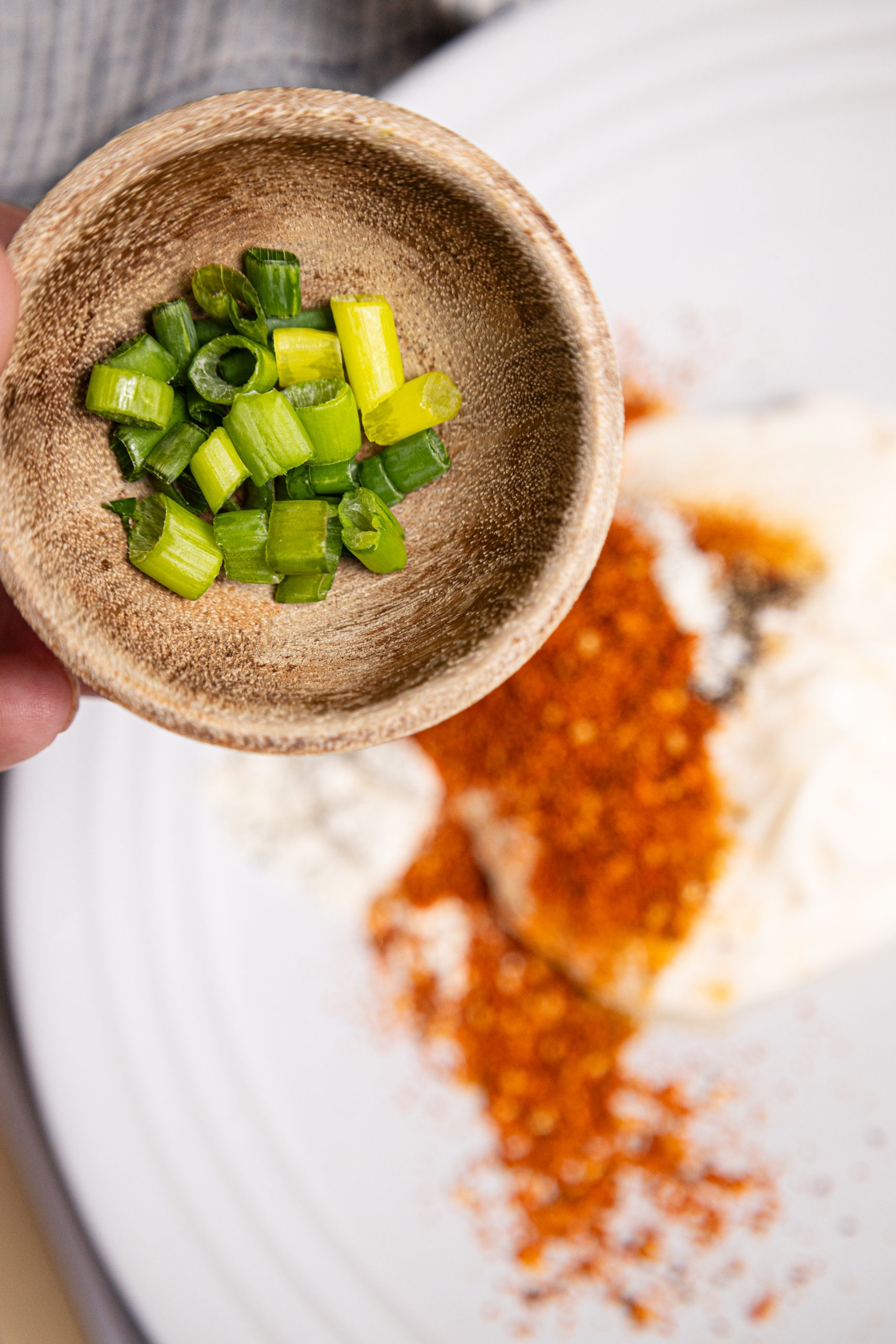 A person is holding a small bowl of peppers on a plate.