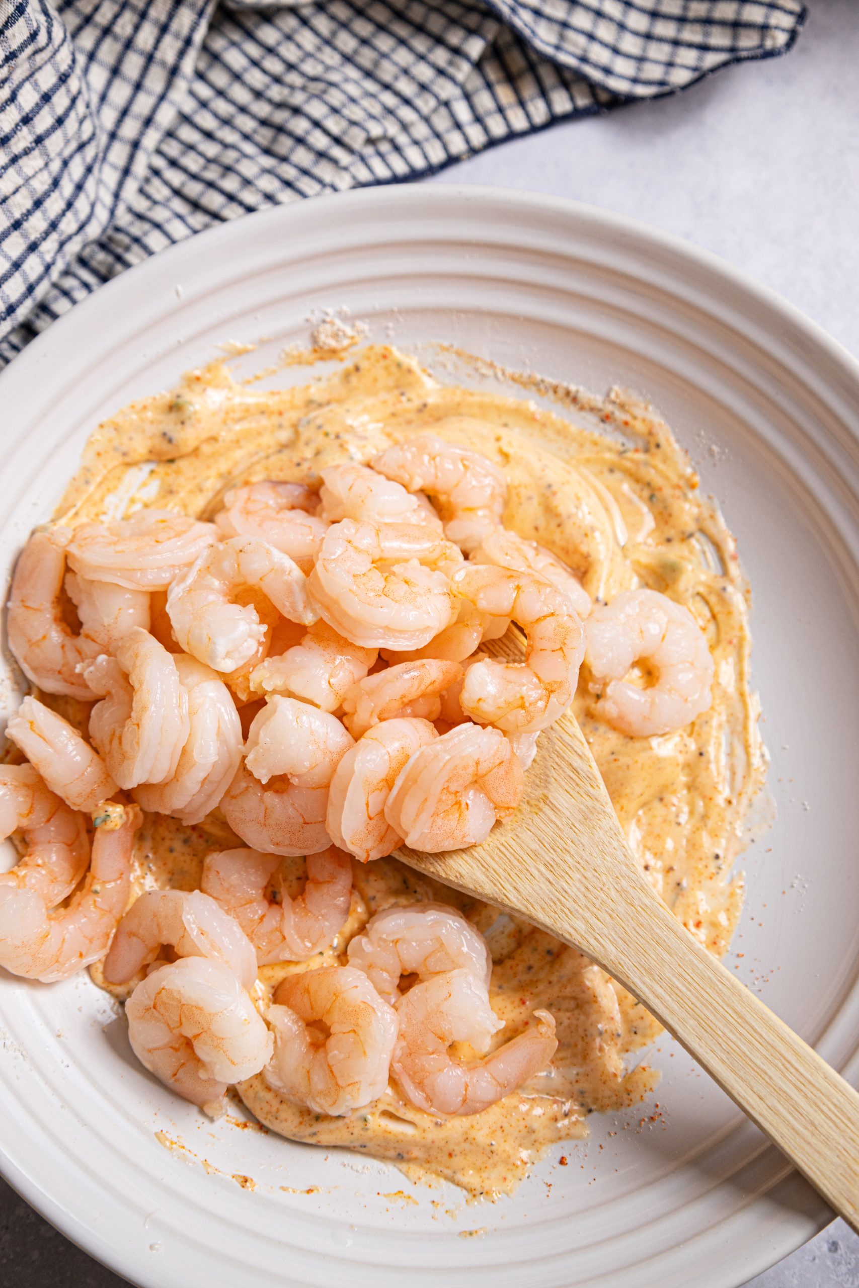 Shrimp on a white plate with a wooden spoon.