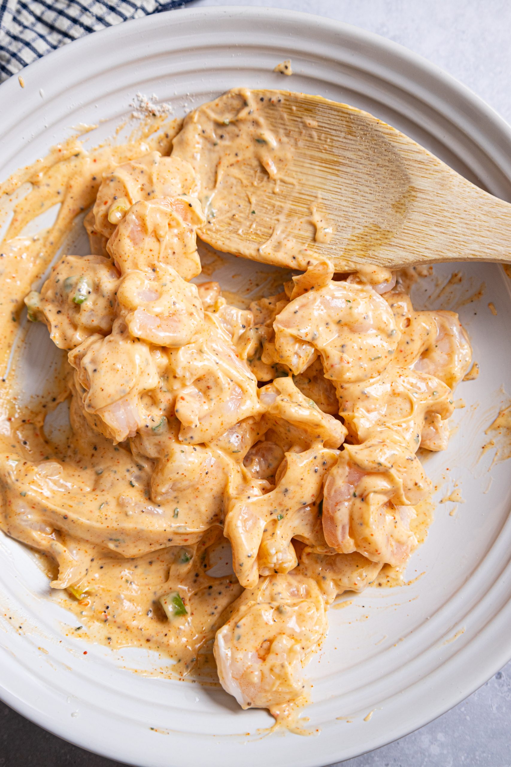 A white plate with shrimp in a sauce with a wooden spoon.