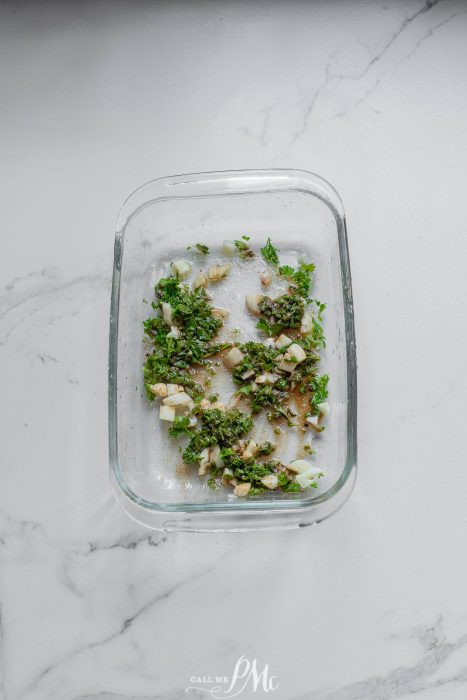 A glass bowl filled with herbs on a marble countertop.