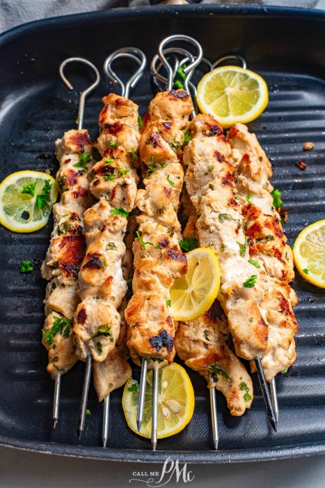 Chicken skewers on a black pan with lemon wedges.