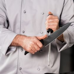 A chef is holding a knife in front of a kitchen. Discover the best kitchen knives.